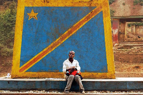 Uomo seduto davanti alla bandiera della R.D. Congo